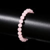 A close-up of a natural pink quartz stretch bracelet worn on a wrist against a dark background.