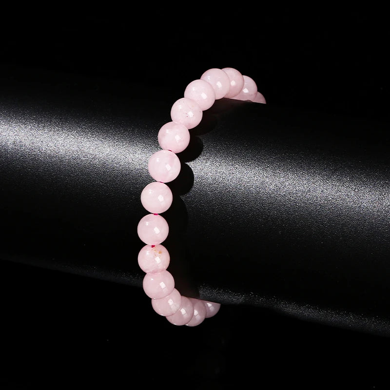 A close-up of a natural pink quartz stretch bracelet worn on a wrist against a dark background.