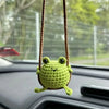 Handmade crochet green frog charm hanging from a brown string on a car interior