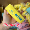 A hand holds a yellow butter stick squishy stress ball with salted butter visible in the background.