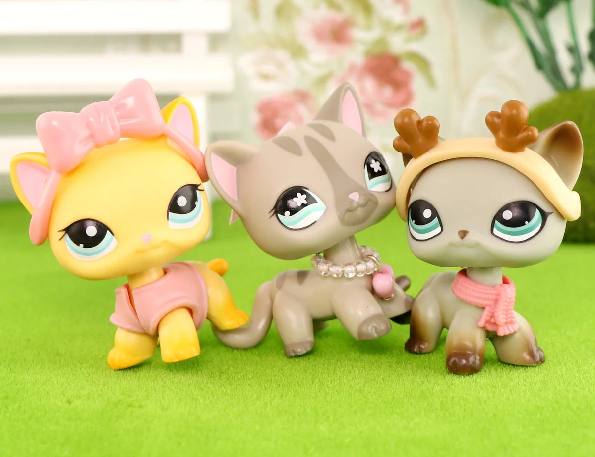A set of three pastel-colored LPS-style vinyl cat figurines with scarf necklace accessories sitting on green grass.