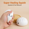 A hand squeezes a white squishy stress ball with a cute face, next to a yellow silicone mold.