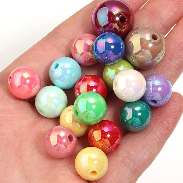 A hand holds several round, iridescent acrylic spacer beads in various shades of pink, green, and purple.