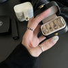 A hand holds an open black leather jewelry storage box displaying various silver and gold rings and earrings.