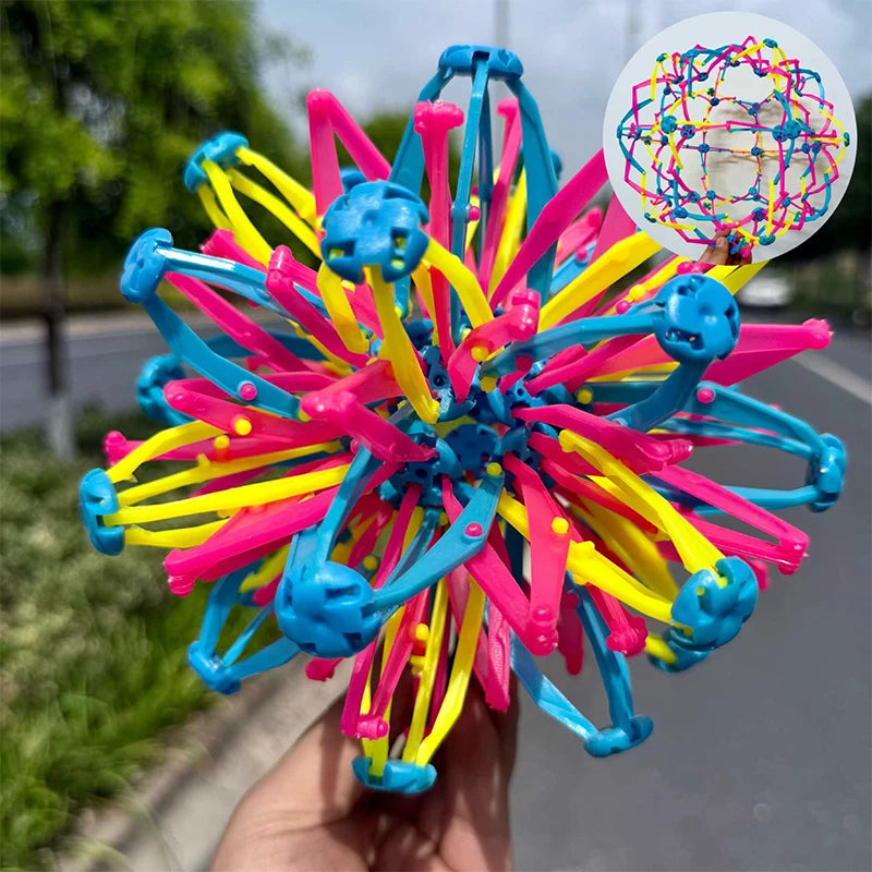 A hand holds an expandable magic ball toy with bright pink, blue, and yellow streamers and a circular diagram.