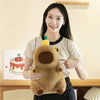 A woman holds a brown capybara plush toy with a small green accessory.