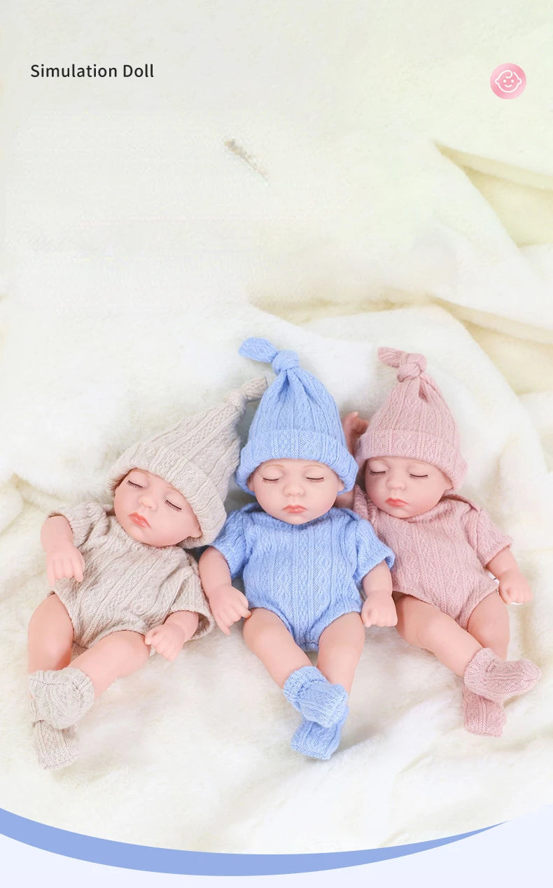 Three newborn simulation dolls wearing knitted outfits in soft pastel colors on a white fluffy surface.