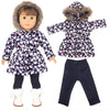 A doll wearing a dark blue and pink floral winter coat dress with a fur hood and black leggings.