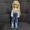 A blonde doll wearing a white shirt and denim jeans with butterfly wings, posing on a dark gray fabric background.
