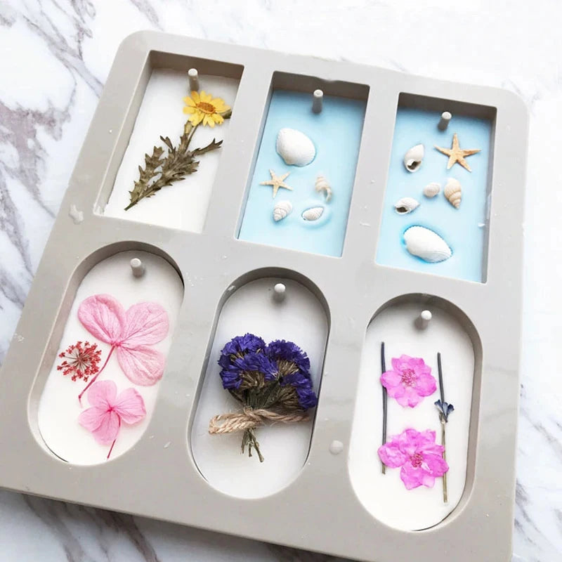 A silicone mold tray with six compartments containing various natural elements like flowers, stones, and botanicals for craft