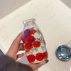 A hand holds a clear glass bottle filled with various colorful fruit pieces used as a squishy fidget toy.