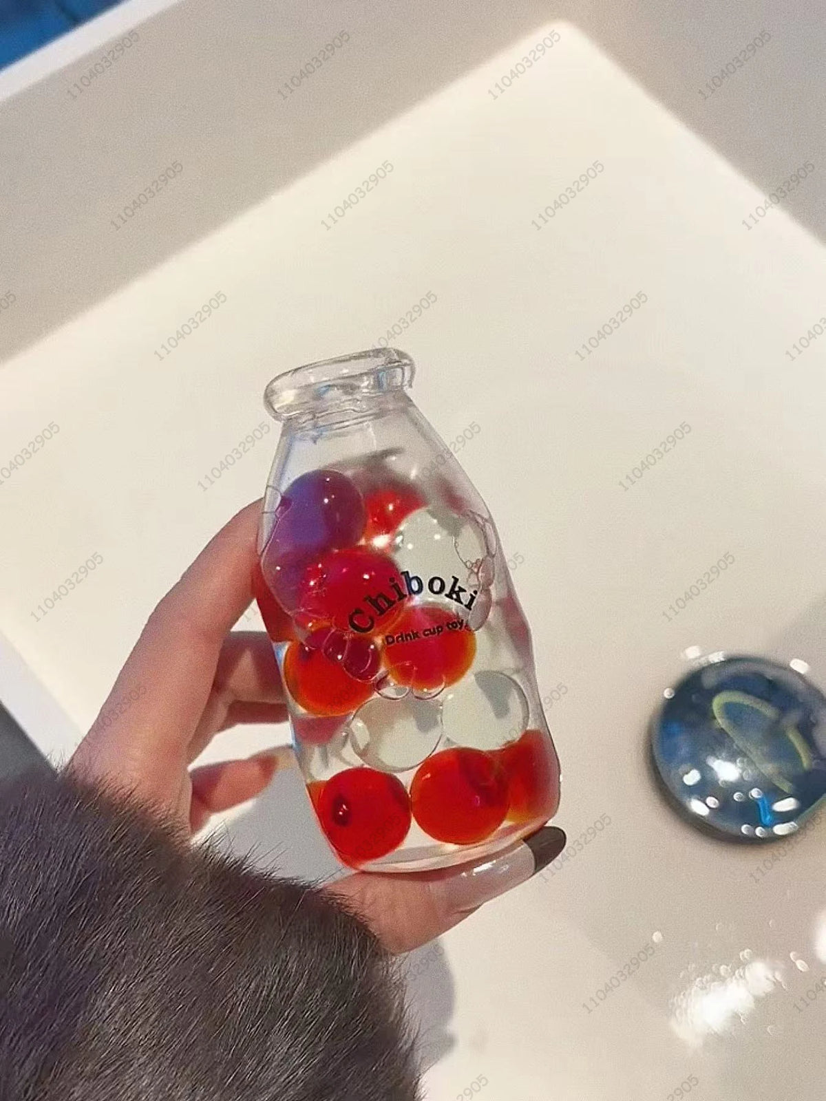 A hand holds a clear glass bottle filled with various colorful fruit pieces used as a squishy fidget toy.