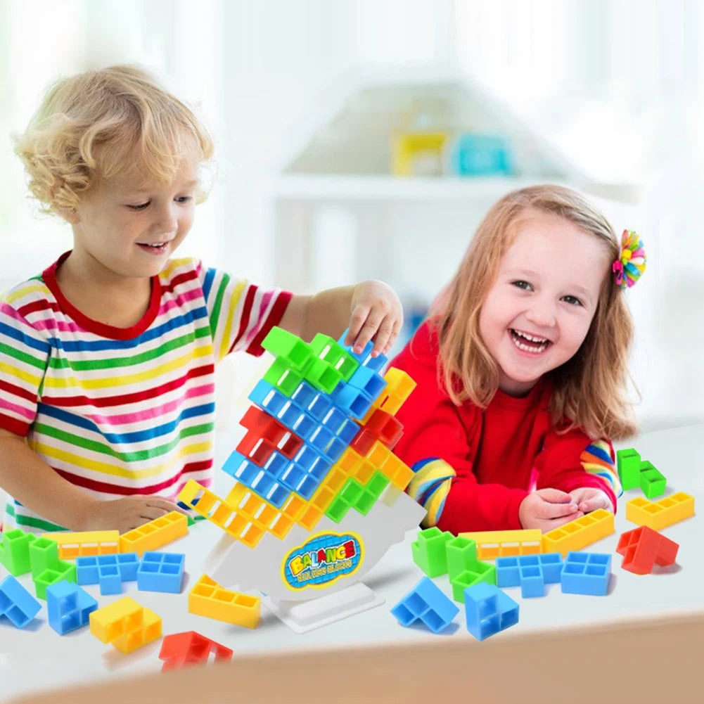 Two young children play with a set of colorful stacking blocks for a balance game.