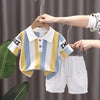 A boy's striped yellow and blue cotton summer short sleeve t-shirt and matching shorts set hanging on a wooden hanger.