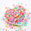 A white bowl filled with colorful polymer clay sprinkles for slime and craft decor, scattered on a white surface.