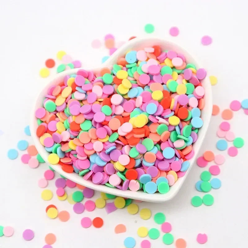 A white bowl filled with colorful polymer clay sprinkles for slime and craft decor, scattered on a white surface.