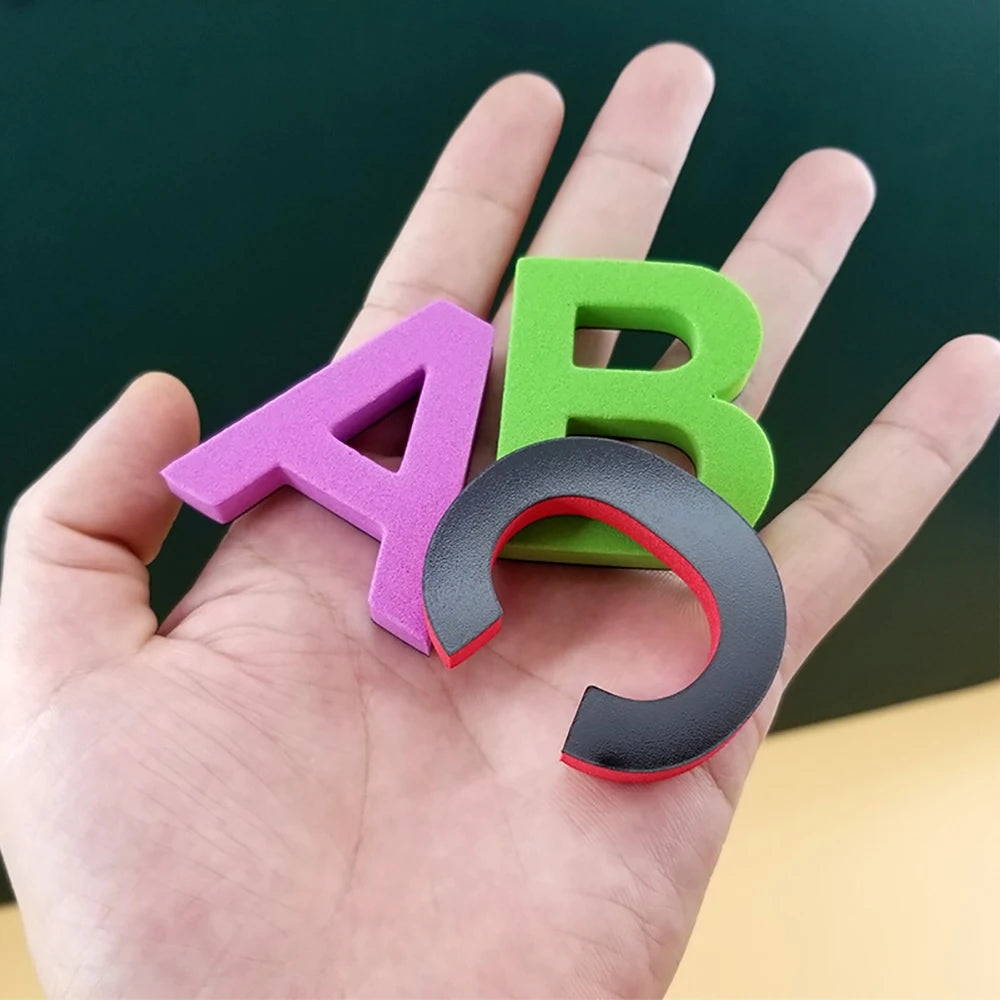 A hand holds three magnetic letters A, B, and a curved letter, all in purple, green, and black.