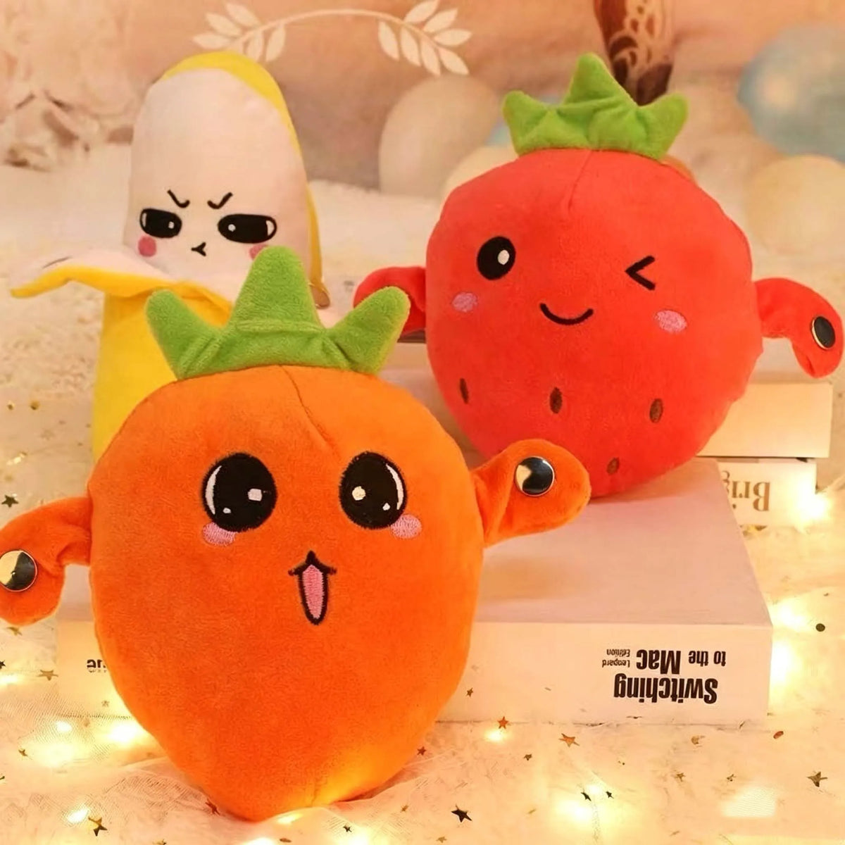 An orange strawberry plush toy next to a yellow fruit plush toy on a white surface.