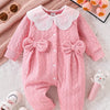 Pink quilted baby girl romper with a lace collar lying on a white textured surface.