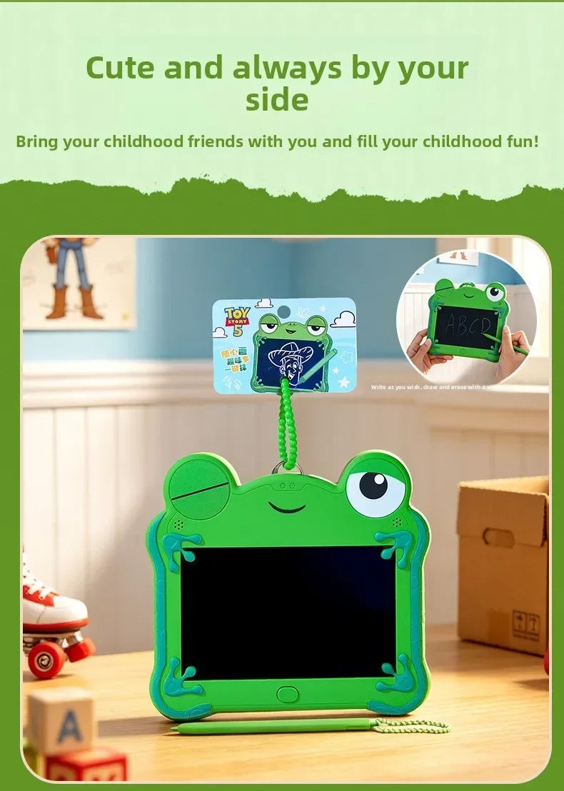 A green frog-shaped LCD drawing tablet keychain with an eraser and a screen is shown on a wooden table.
