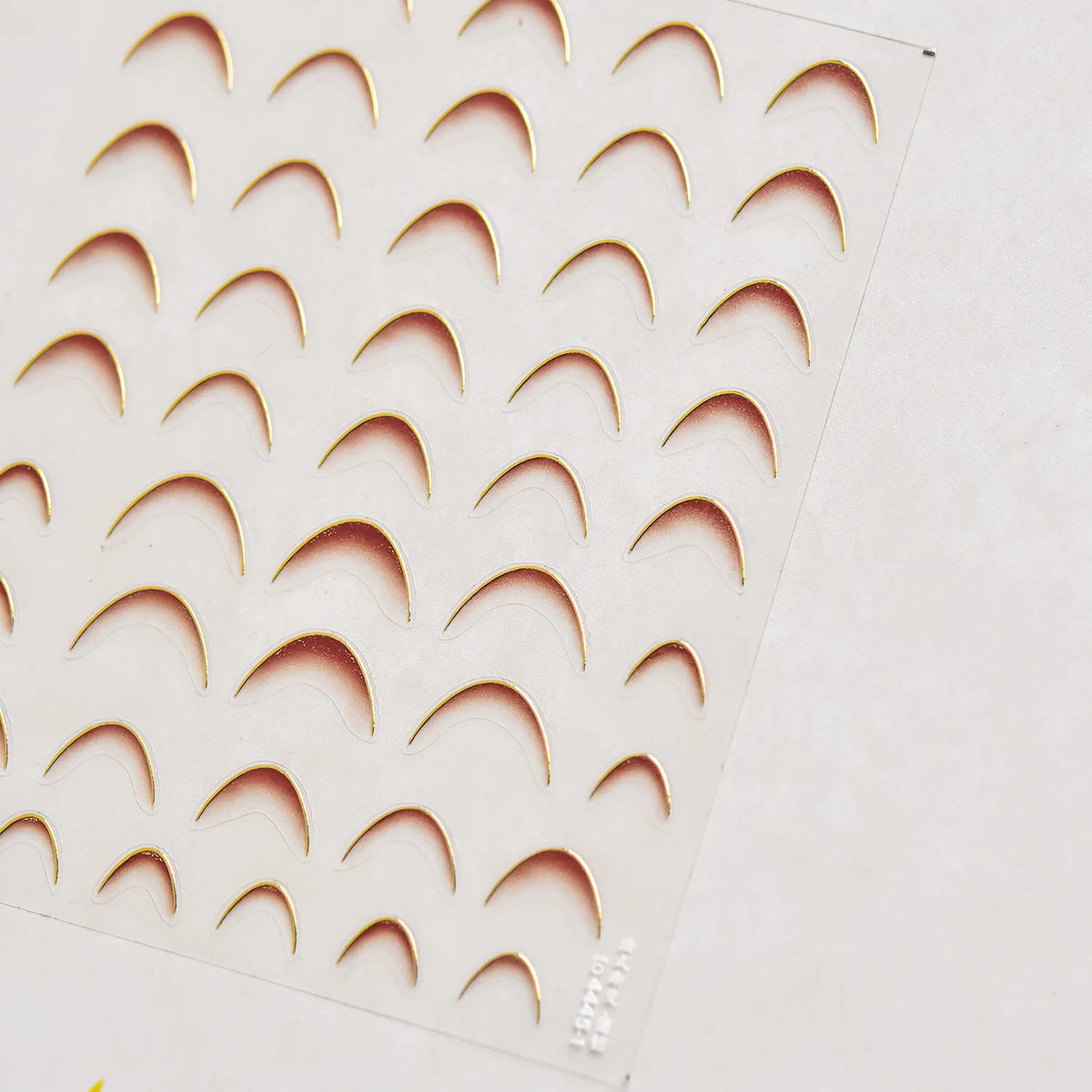 A sheet of gold-colored nail art stickers featuring various curved shapes for cosmetic application.