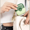 A hand holds a small, light green and white 2-in-1 baby hair cutting comb attached to a cream-colored leather pouch.