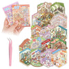 A hand holds a colorful DIY 3D sticker scene book craft kit featuring miniature buildings and landscapes.