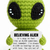 Handmade crochet green alien plush toy with large black eyes and a sign encouraging acceptance of feeling alien