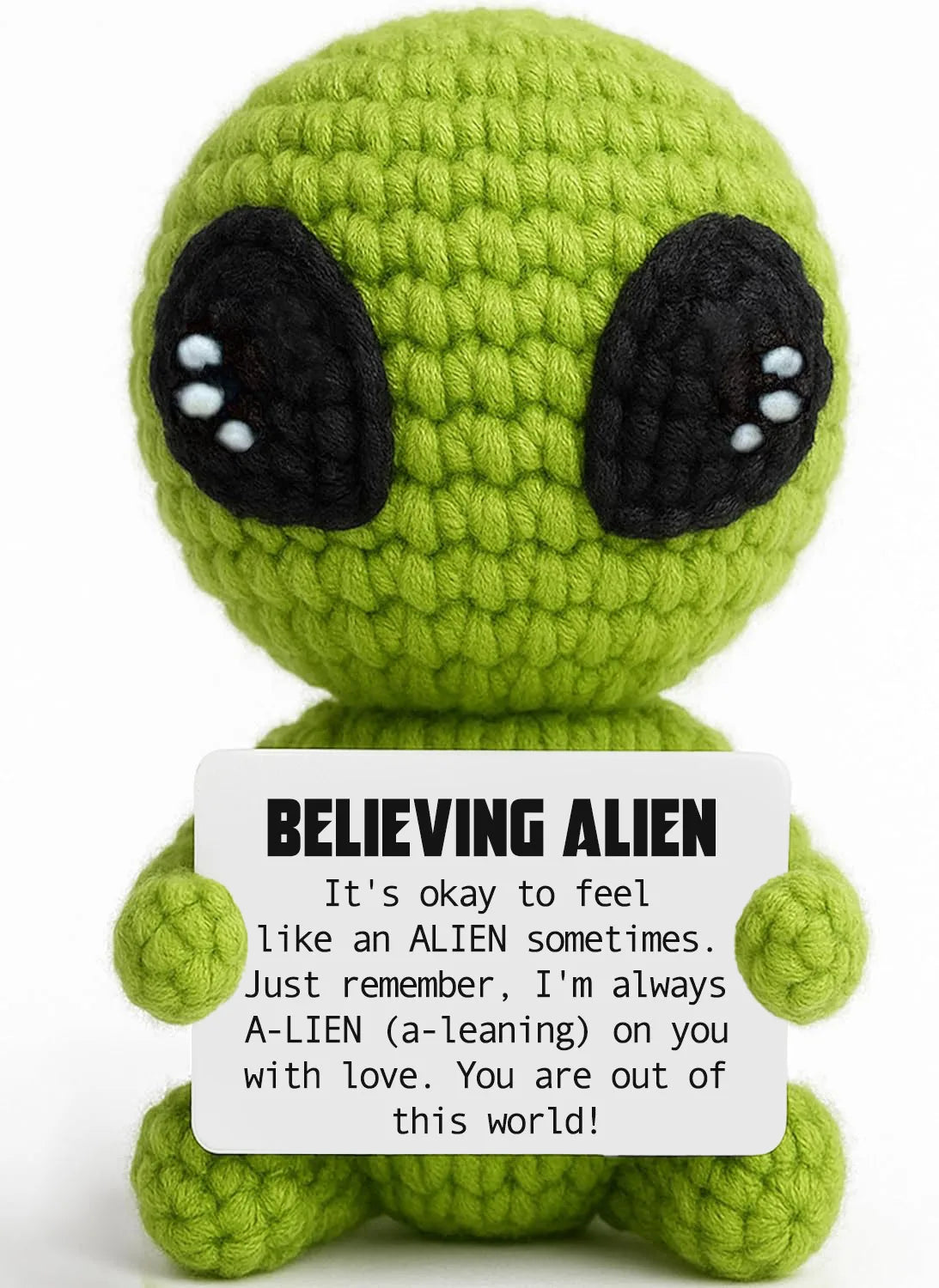 Handmade crochet green alien plush toy with large black eyes and a sign encouraging acceptance of feeling alien
