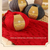 A close-up of three skeins of merino wool yarn in gray, black, and red, displayed on a textured surface.