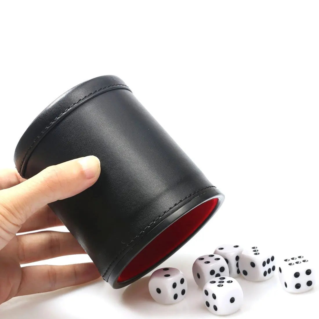 A hand holds a black leather dice cup with a red lining and five white dice on a white surface.