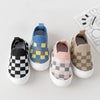 A collection of five plaid slip-on toddler shoes in various colors and patterns, including black and white checkered, blue an
