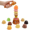 A hand is holding an orange ice cream cone, with various colorful ice cream scoops and toppings scattered around.