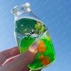A hand holds a clear bottle filled with green liquid, labeled Chiboki, against a blue sky.