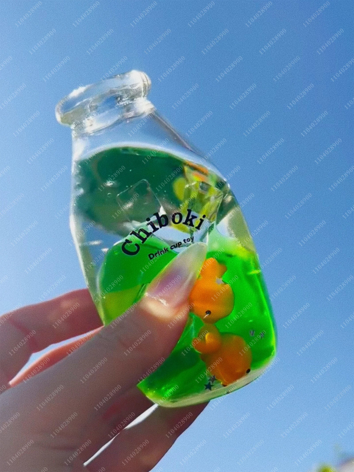 A hand holds a clear bottle filled with green liquid, labeled Chiboki, against a blue sky.