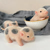 A soft pink silicone reborn piglet doll is shown in a bowl on a gray fabric surface.