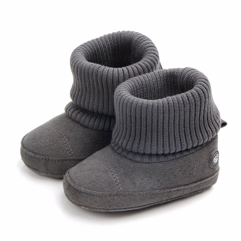 A pair of gray baby winter snow boots with fuzzy ball accents shown from the side.