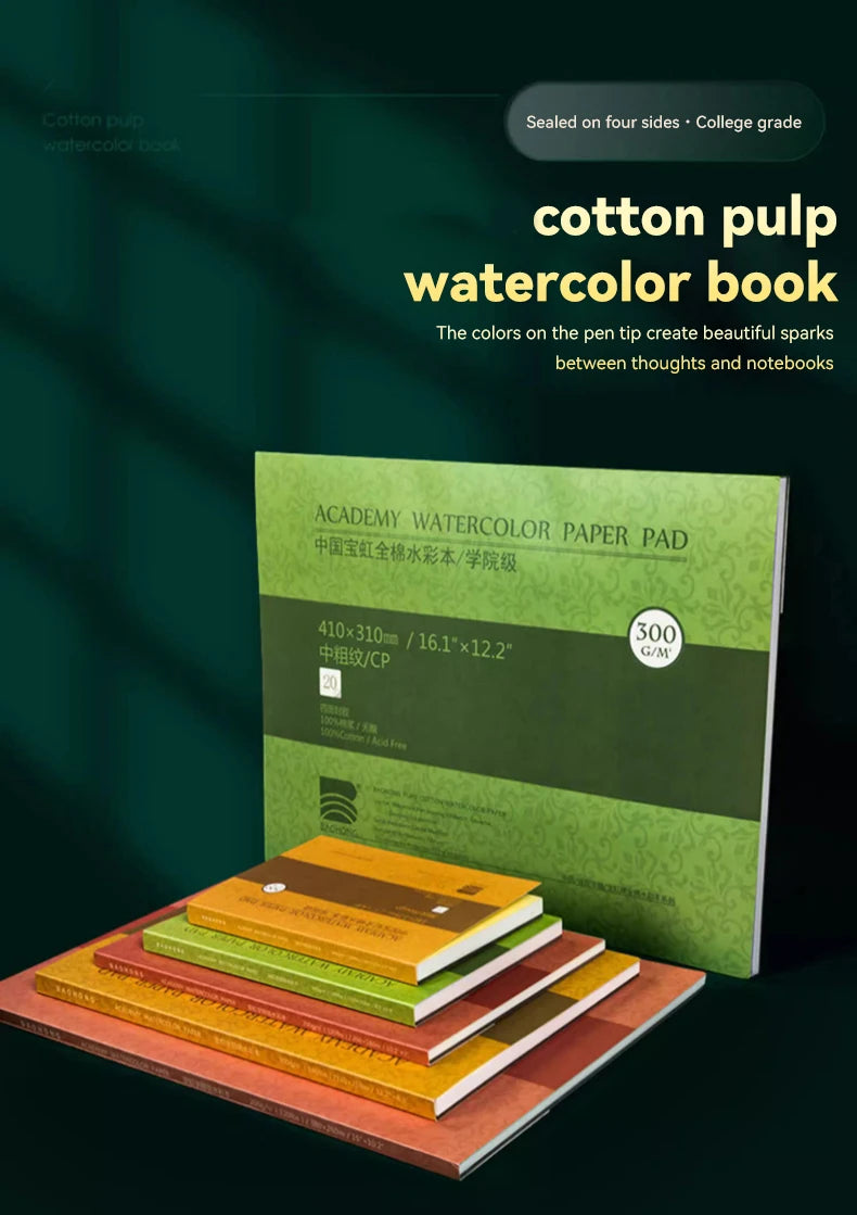 A stack of watercolor paper pads and a green watercolor book are displayed on a dark surface.
