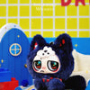 A fluffy dark blue creature with large eyes is featured against a yellow grid background.