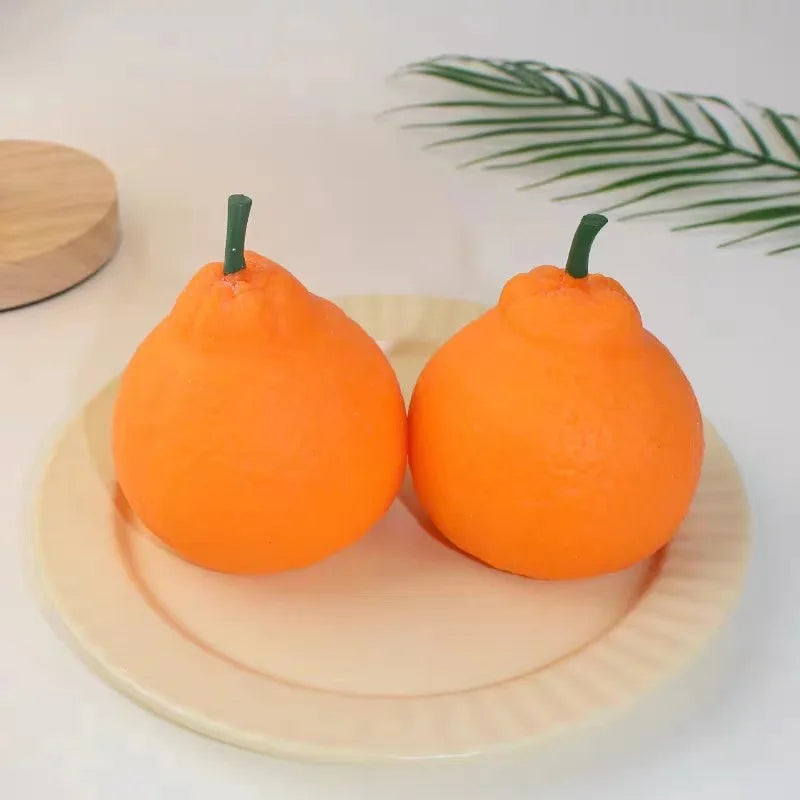 An orange fruit squishy stress relief fidget toy resting on a light yellow plate with a green palm leaf in the background.