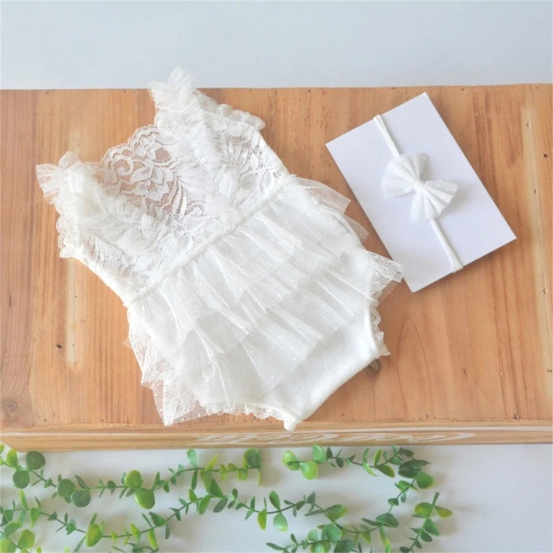 White lace baby romper with ruffled details and a matching white bow headband on a wooden surface.