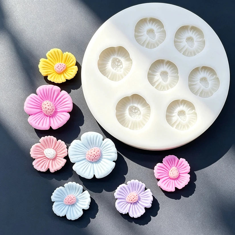 A silicone mold with multiple daisy flower shapes in pink, purple, and blue colors is shown on a dark surface.
