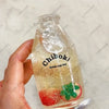 A clear glass bottle filled with yellowish liquid and fruit pieces is held in a hand.