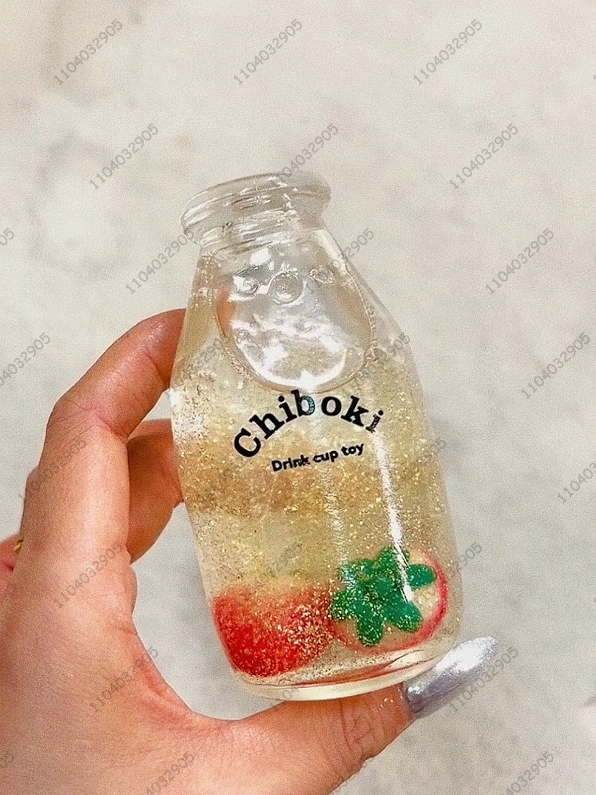 A clear glass bottle filled with yellowish liquid and fruit pieces is held in a hand.