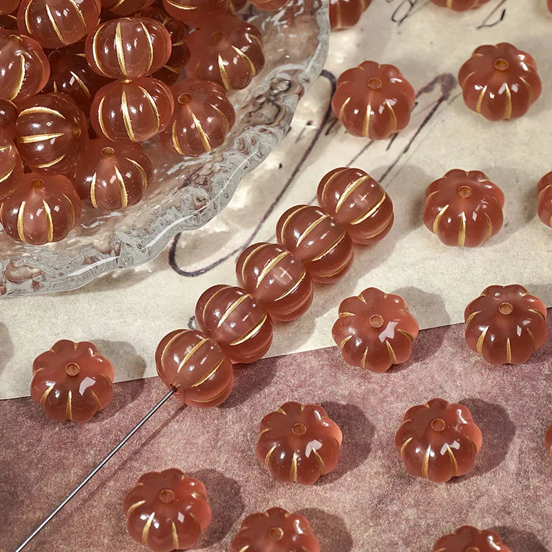 A collection of small, reddish-brown pumpkin-shaped resin beads with gold tracing for jewelry making.