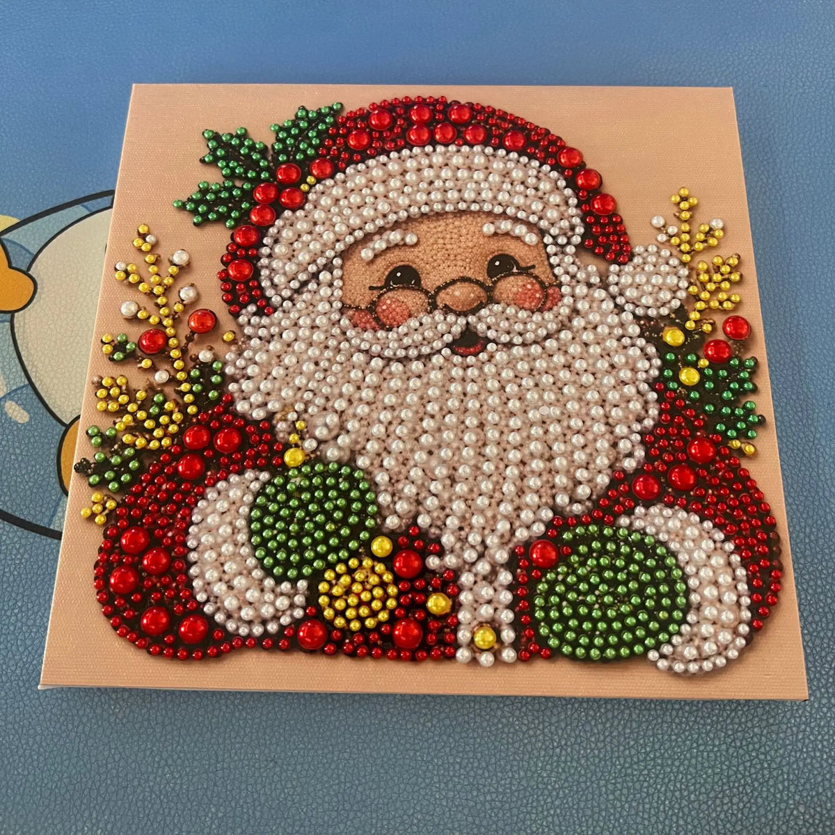 A detailed painting of Santa Claus with a white beard and red hat made from various pearl beads on a canvas.