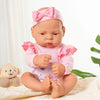 A lifelike vinyl reborn doll with a pink bow and outfit sitting on a white surface.