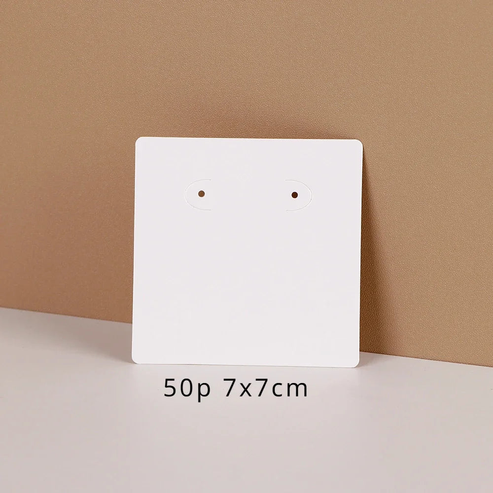 A white square jewelry display card with two small holes is shown against a beige background.