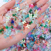 A hand holds a mix of multicolor aurora resin nail charms, featuring iridescent pinks, blues, greens, and purples.