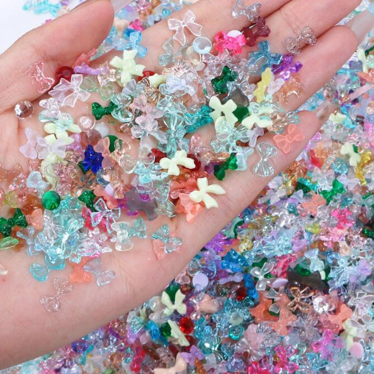 A hand holds a mix of multicolor aurora resin nail charms, featuring iridescent pinks, blues, greens, and purples.